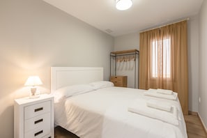 Habitació d'hotel amb un llit individual, una taula de nit amb una làmpada, una petita taula de nit de fusta i una finestra amb cortines.