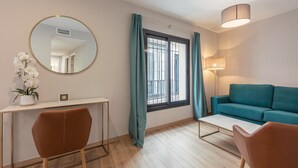 Een moderne woonkamer met een blauwgroene bank, een ronde spiegel, een bureau met stoel, en een raam met gordijnen.