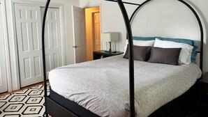 A four-poster bed with a patterned bedspread, a bedside table with a lamp, and a geometric patterned rug.