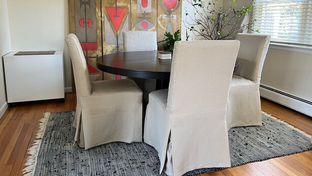 A dining area with a round table, four chairs, a patterned rug, and a decorative wall panel.