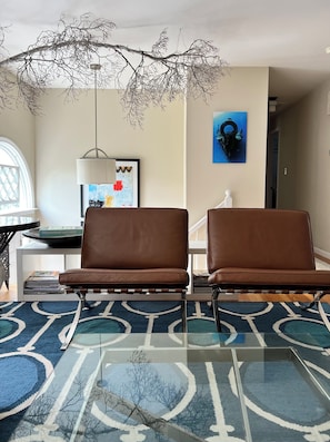 A room with two brown leather chairs, a blue patterned rug, a framed abstract painting, and a hanging branch decoration.