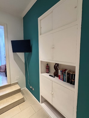 Ein Zimmer mit Türkiswänden, einem weißen Schrank mit Büchern, einem an der Wand befestigten Fernseher und einer Treppe.