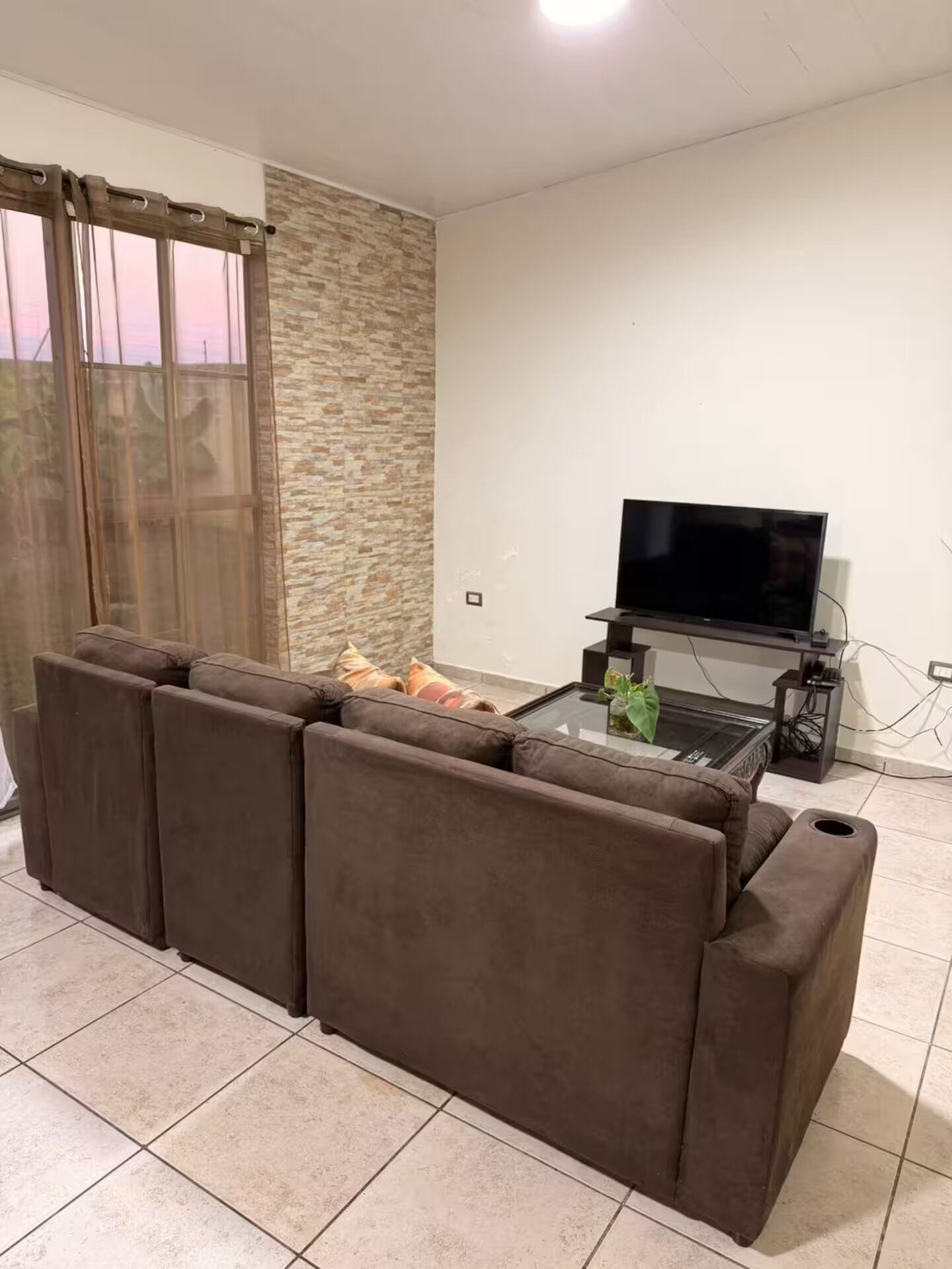 Een woonkamer met een hoekbank, een flatscreen televisie op een meubel en een glazen salontafel.