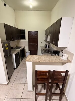 A compact kitchen with a central island, dark cabinets, and a tiled floor. - Moderno apartamento urbano de 2 habitaciones / aire acondicionado / piscina (Nejapa)