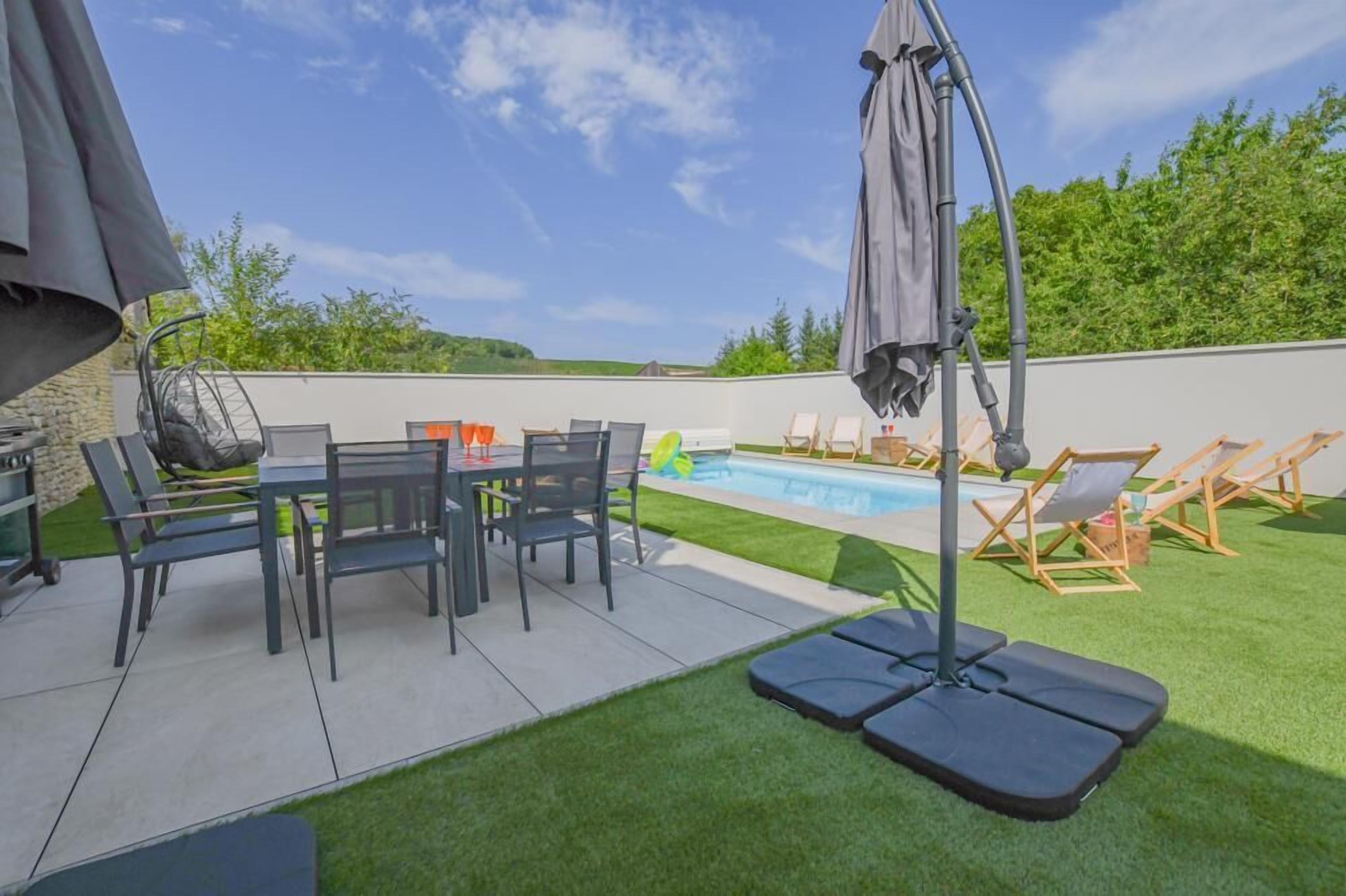 A backyard with a pool, a dining table with chairs, and lounge chairs.