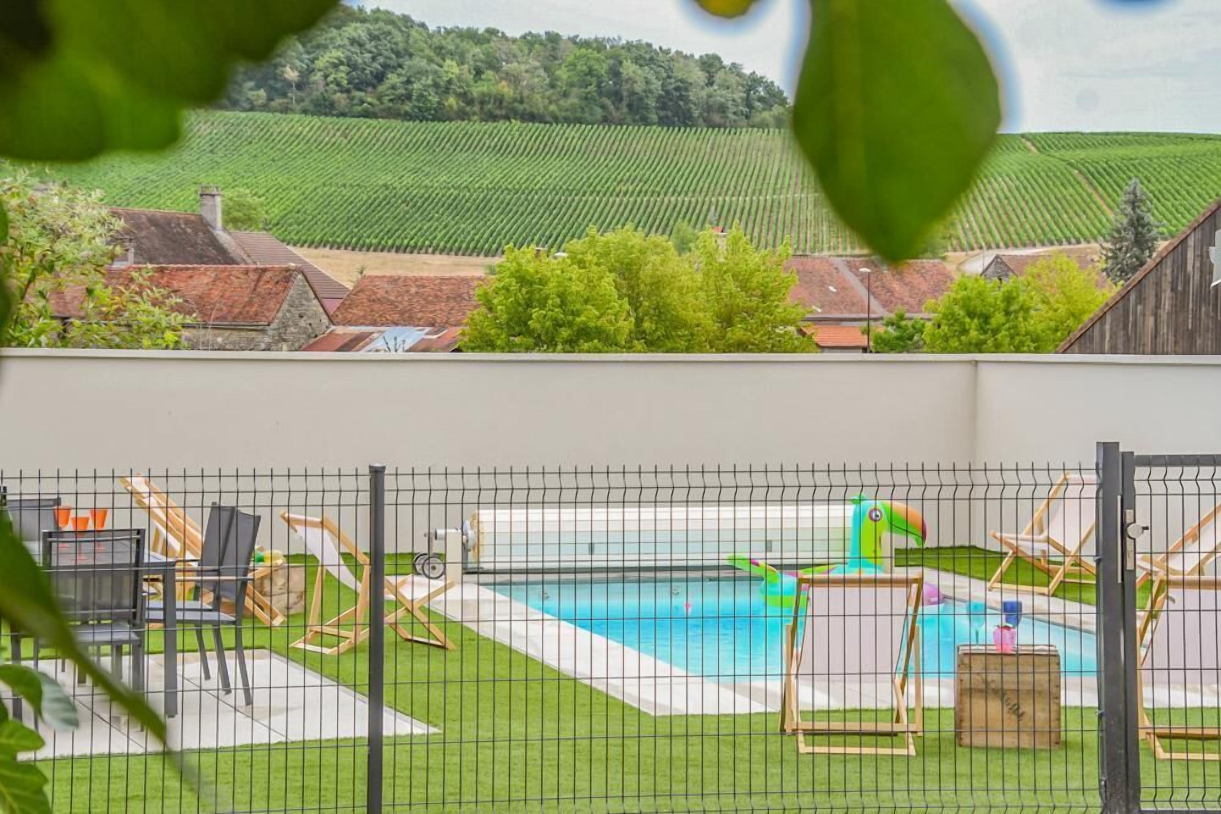 A backyard with a swimming pool, surrounded by a fence, and a view of a vineyard in the background.
