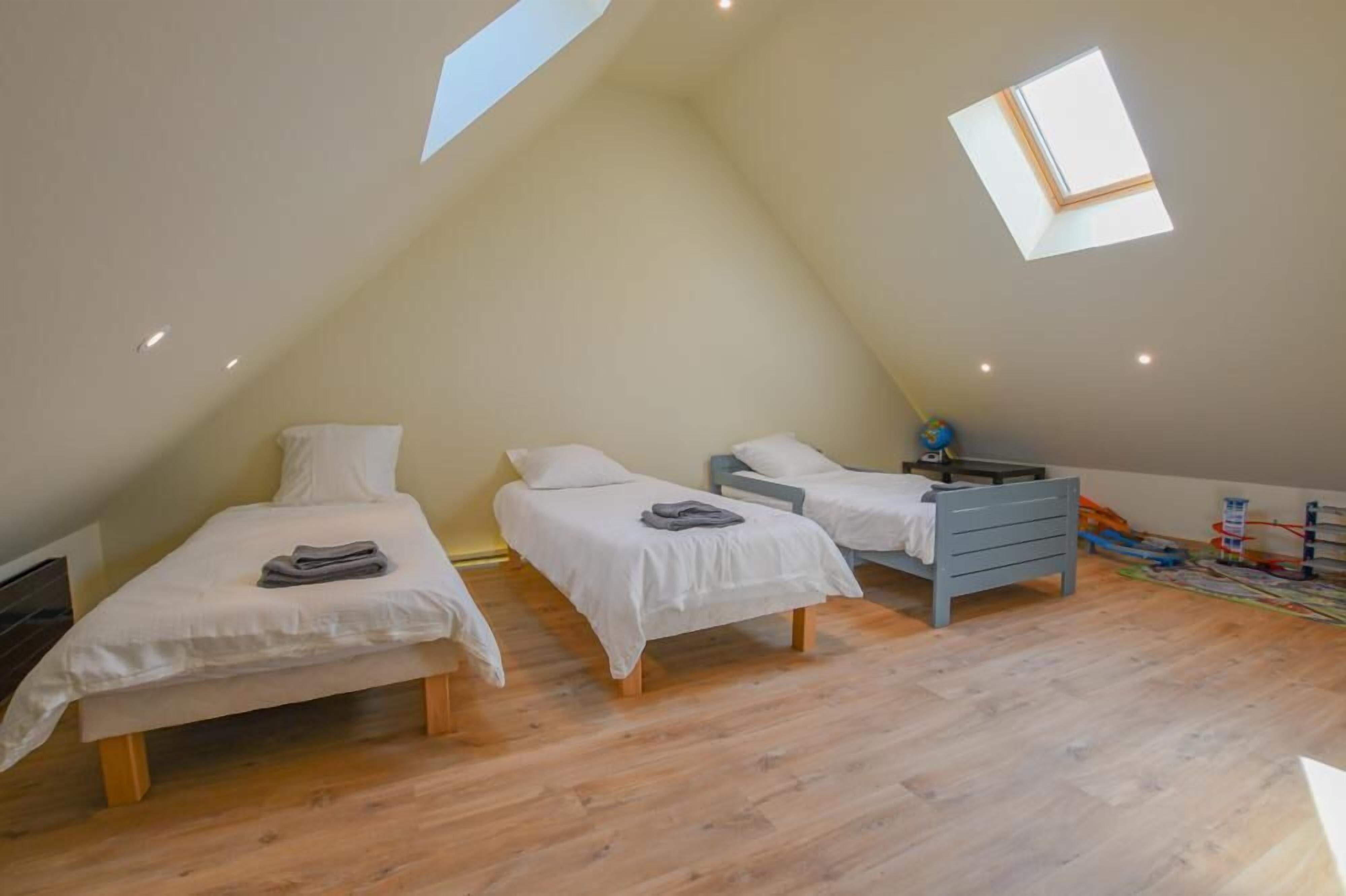 A triangular room with three beds arranged in a row, wooden flooring, and a skylight.