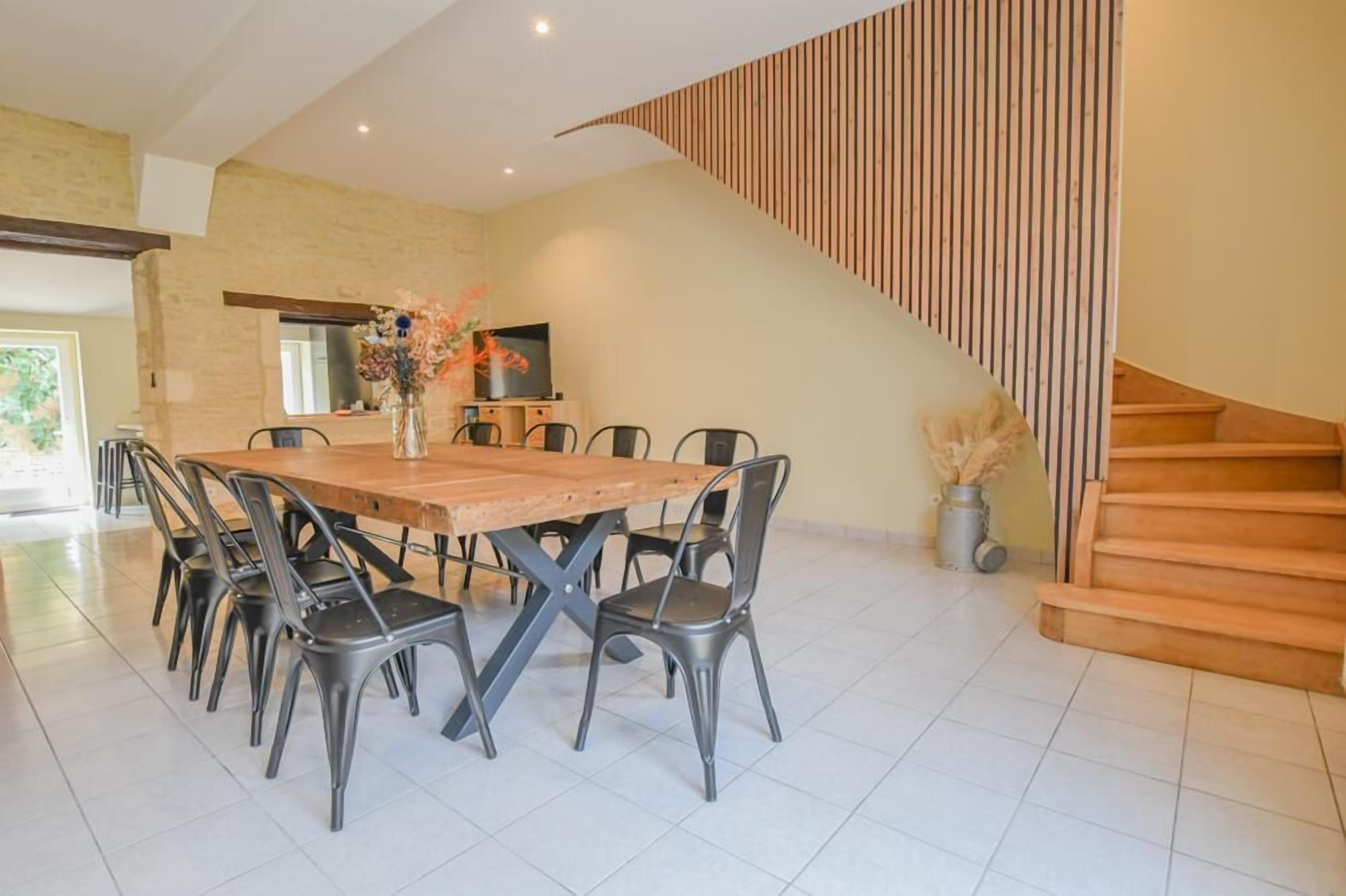A dining area with a wooden table and metal chairs, a staircase, and a decorative vase with flowers.