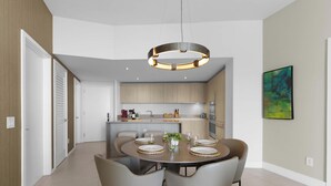 Et moderne køkken med en central ø, loftslamper og et spiseområde med et rundt bord og stole.