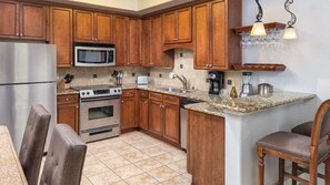 A kitchen with wooden cabinets, stainless steel appliances, a granite countertop, and a bar stool. - Sip, Savor & Stay in Style — A Wine Country Escape- Wyndham Vino Bello- 1 Bd. (Napa)
