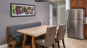 A dining area with a bench, chairs, a table, a refrigerator, and a framed picture on the wall. - Sip, Savor & Stay in Style — A Wine Country Escape- Wyndham Vino Bello- 1 Bd. (Napa)