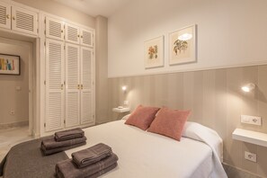 A bedroom with a bed, two pillows, a nightstand, a wall-mounted light, a framed picture, and a set of closed white doors. - City Centre Apartment with Balcony, Elevator and WiFi (Seville)