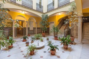 A spacious courtyard with multiple potted plants, a central fountain, and a staircase leading to an upper level. - City Centre Apartment with Balcony, Elevator and WiFi (Seville)