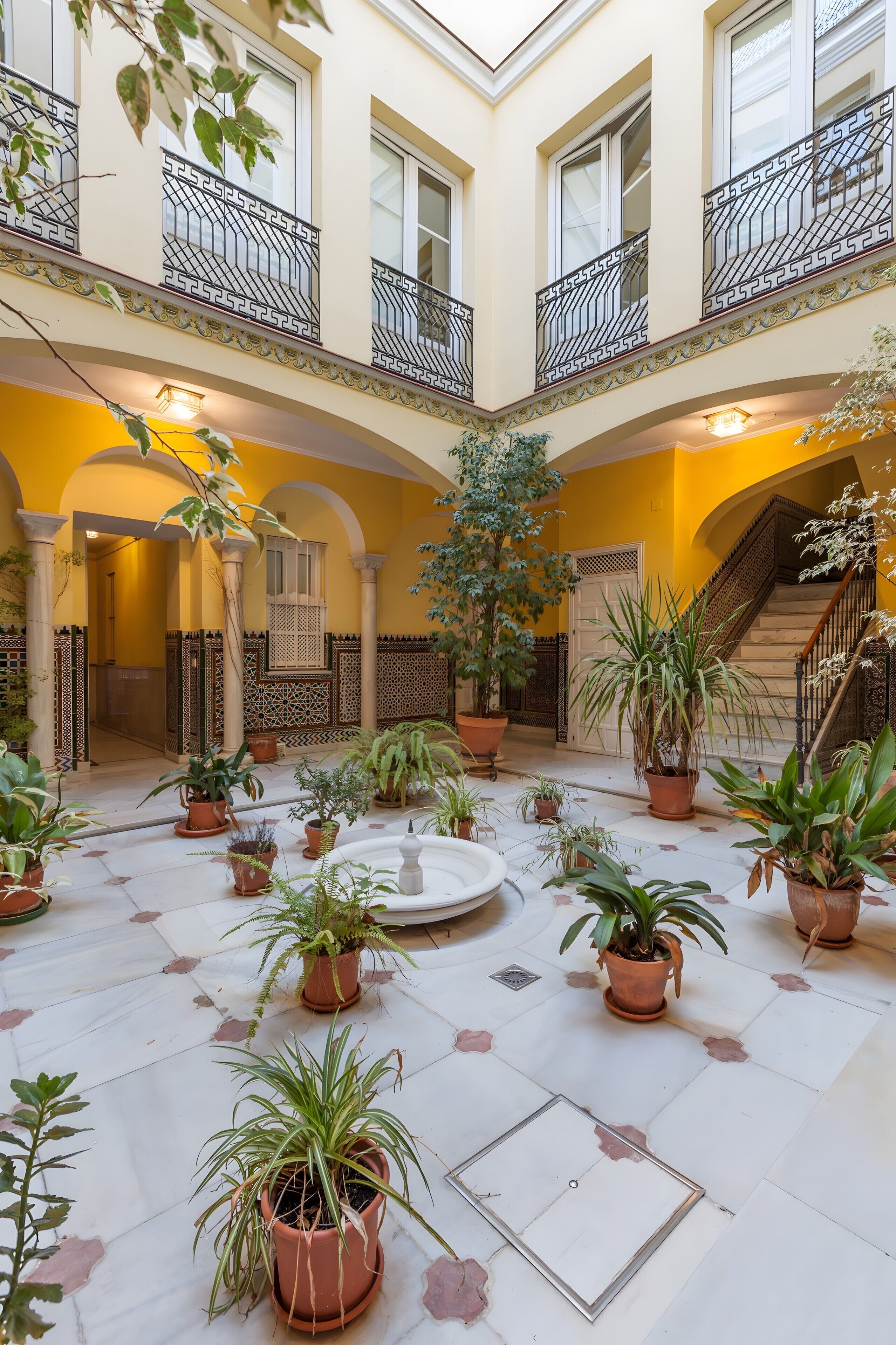 Un patio amplio con numerosas plantas en macetas, una fuente y una escalera que conduce a un nivel superior.