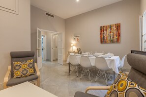 A dining area with a table set for six, a sofa, and a chair with a patterned cushion. - City Centre Apartment with Balcony, Elevator and WiFi (Seville)