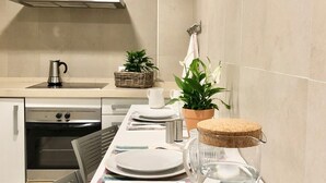 A modern kitchen with a stainless steel range hood, a built-in oven, and a dining area set with plates, cutlery, and a glass jar. - Cozy and Quiet City Centre Apartment with WiFi (Seville)