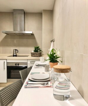 A modern kitchen with a stainless steel range hood, a built-in oven, and a dining area set with plates, cutlery, and a glass jar. - Cozy and Quiet City Centre Apartment with WiFi (Seville)