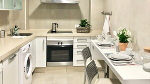 A modern kitchen with a built-in oven, a washing machine, and a dining area with chairs and a table set for two. - Cozy and Quiet City Centre Apartment with WiFi (Seville)