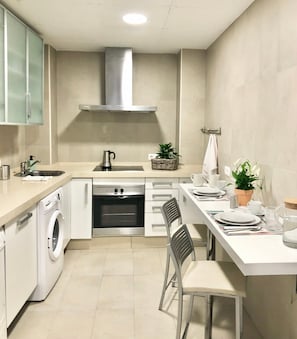 A modern kitchen with a built-in oven, a washing machine, and a dining area with chairs and a table set for two. - Cozy and Quiet City Centre Apartment with WiFi (Seville)