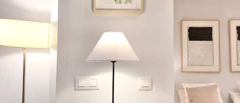 Un dormitorio con una cama, una mesita de noche con lámpara, un cuadro en la pared y un libro sobre la mesa.