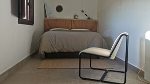 Quarto com cama, cadeira, mesa de cabeceira e prateleira na parede.