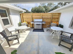 Une terrasse avec un barbecue, des chaises blanches et une clôture en bois.