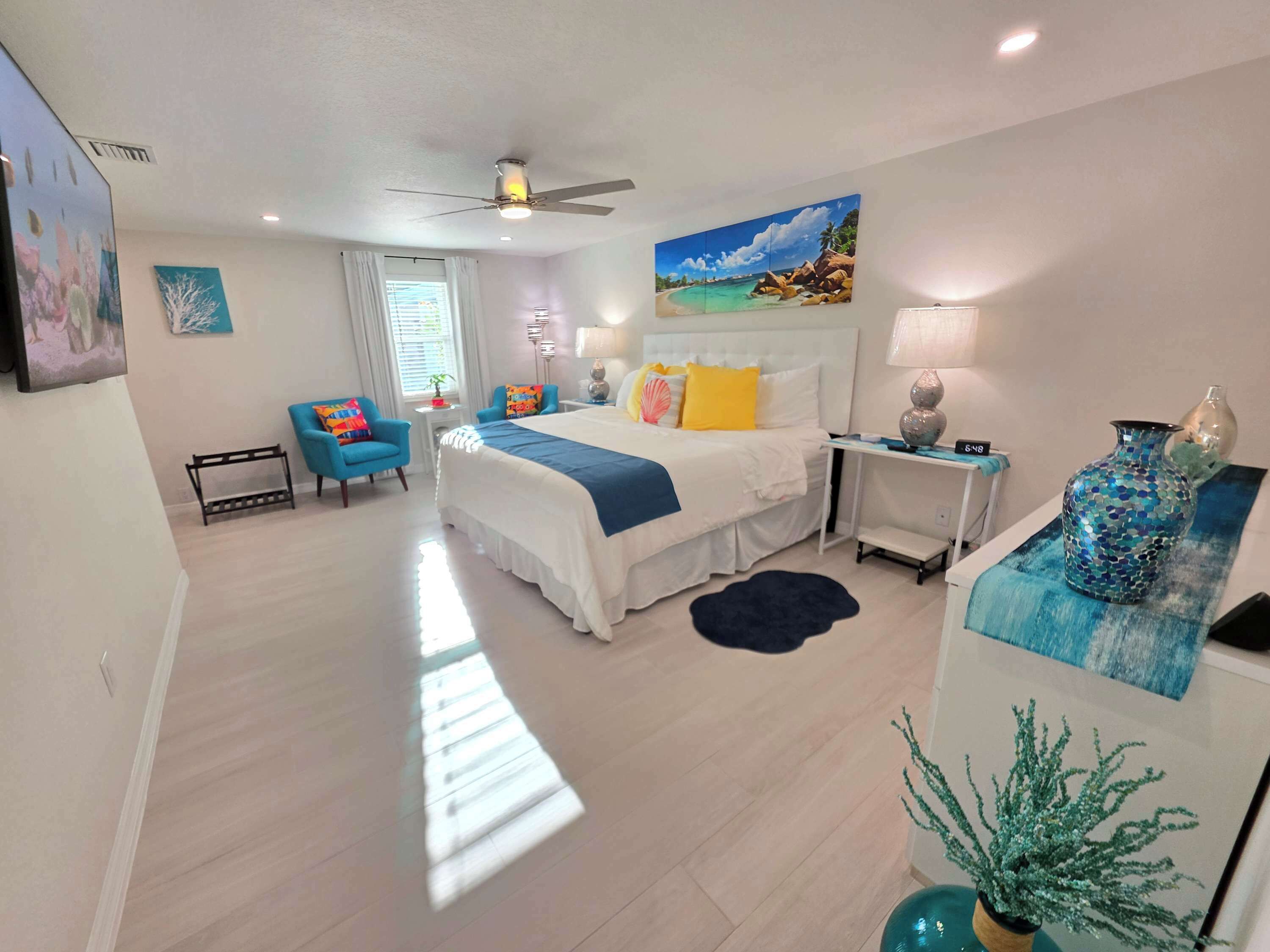 A modern bedroom with a bed, a desk, a chair, and a ceiling fan.