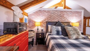 A bedroom with a brick wall, a bed with a plaid blanket, two bedside lamps, a red dresser, and a vintage radio. - Private Ranch - 27 Acres - Two Private, Secluded Cabins (Broken Bow)