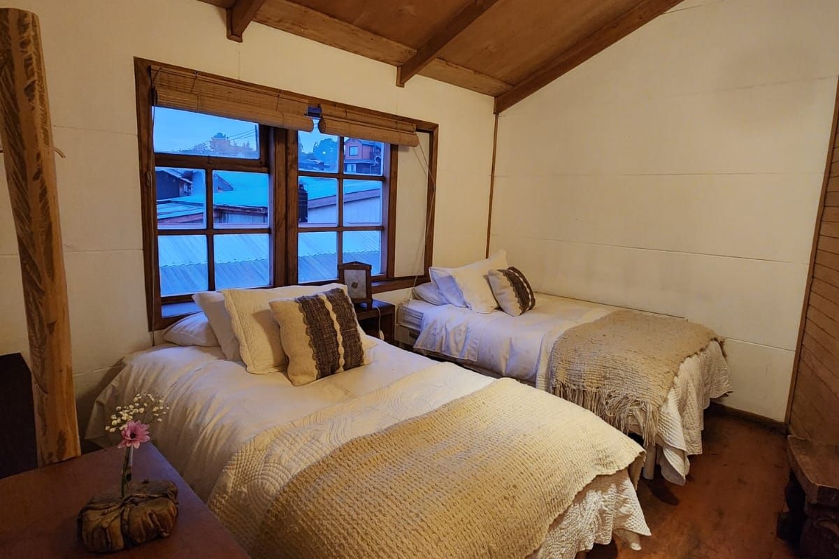 Una habitación acogedora con dos camas, techo de madera, ventana con vistas y una pequeña mesa con un florero.