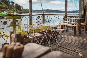 Terraza exterior con mesa y sillas, con vista a un cuerpo de agua.