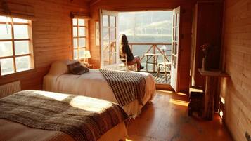 Une chambre dans une cabane en bois, avec un lit, une chaise et une vue sur l’extérieur.