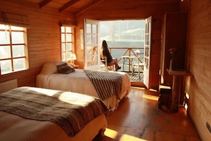 Un dormitorio de cabaña de madera con una cama, una silla y vistas al exterior.