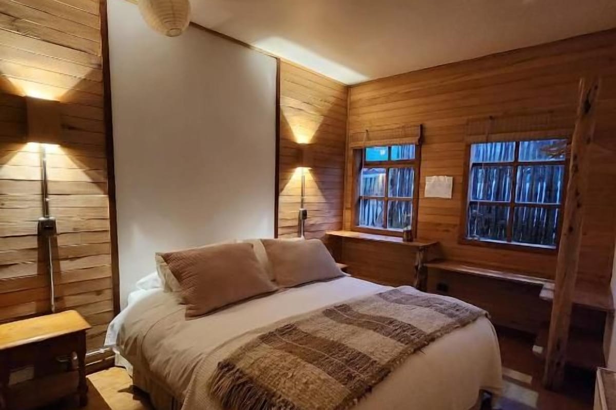 Un dormitorio con una cama grande, paredes de madera y dos ventanas.