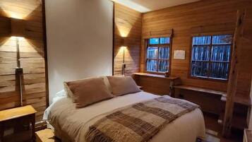 Une chambre à coucher avec un grand lit, des murs en bois et deux fenêtres.