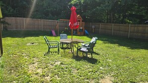 A backyard with a wooden fence, a swing set, a table with chairs, and a red umbrella. - Lakes Region Family Getaway& Pet Friendly (Belmont)