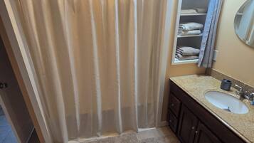 A bathroom with a shower curtain, a sink, a mirror, and a towel rack.