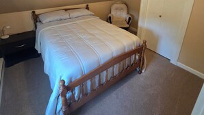 A bedroom with a wooden bed, a chair, a wardrobe, and a ceiling light. - Lakes Region Family Getaway& Pet Friendly (Belmont)