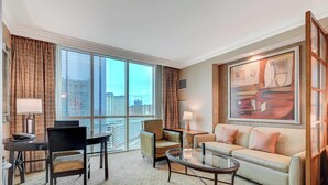 Ein Hotelzimmer mit großem Fenster, einer Couch, einem Couchtisch, einem Schreibtisch und einem Stuhl.