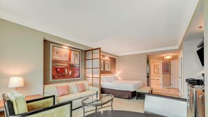 Ein Hotelzimmer mit Bett, einer Couch, einem Glastisch, einer Lampe und Kunstwerken an der Wand.