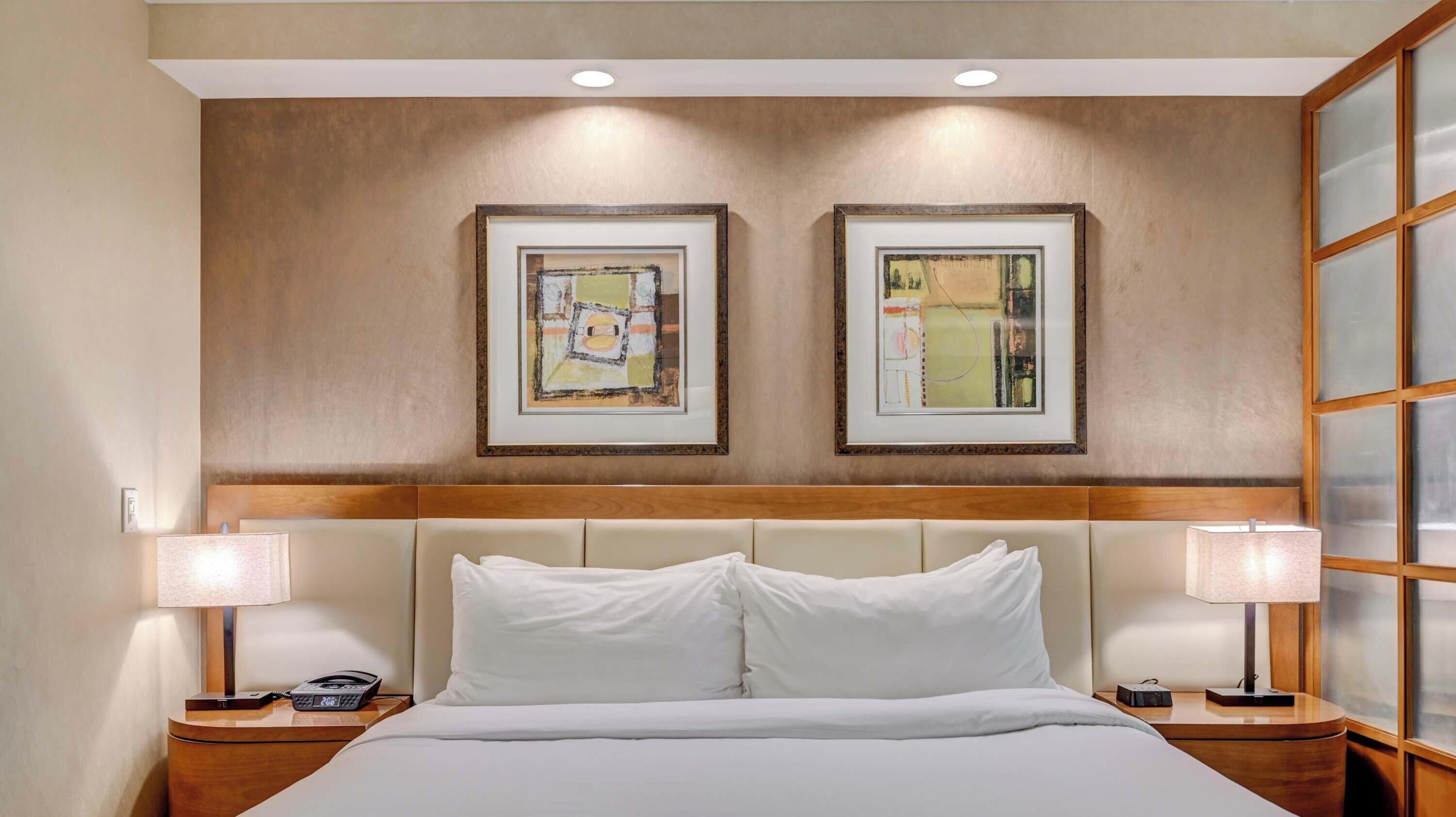 A hotel room with a large bed, two framed artworks on the wall, and a window with a wooden frame.