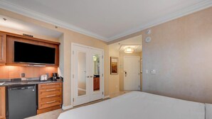 Quarto de hotel com cozinha compacta, uma cama e uma porta que dá para outro espaço.
