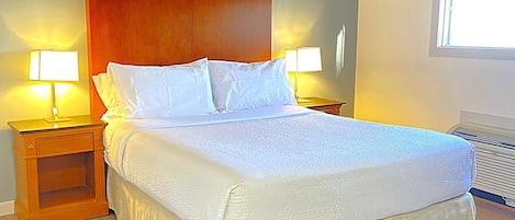 Habitación de hotel con una cama grande, dos mesitas de noche con lámparas, un cabecero de madera y una ventana con persianas.