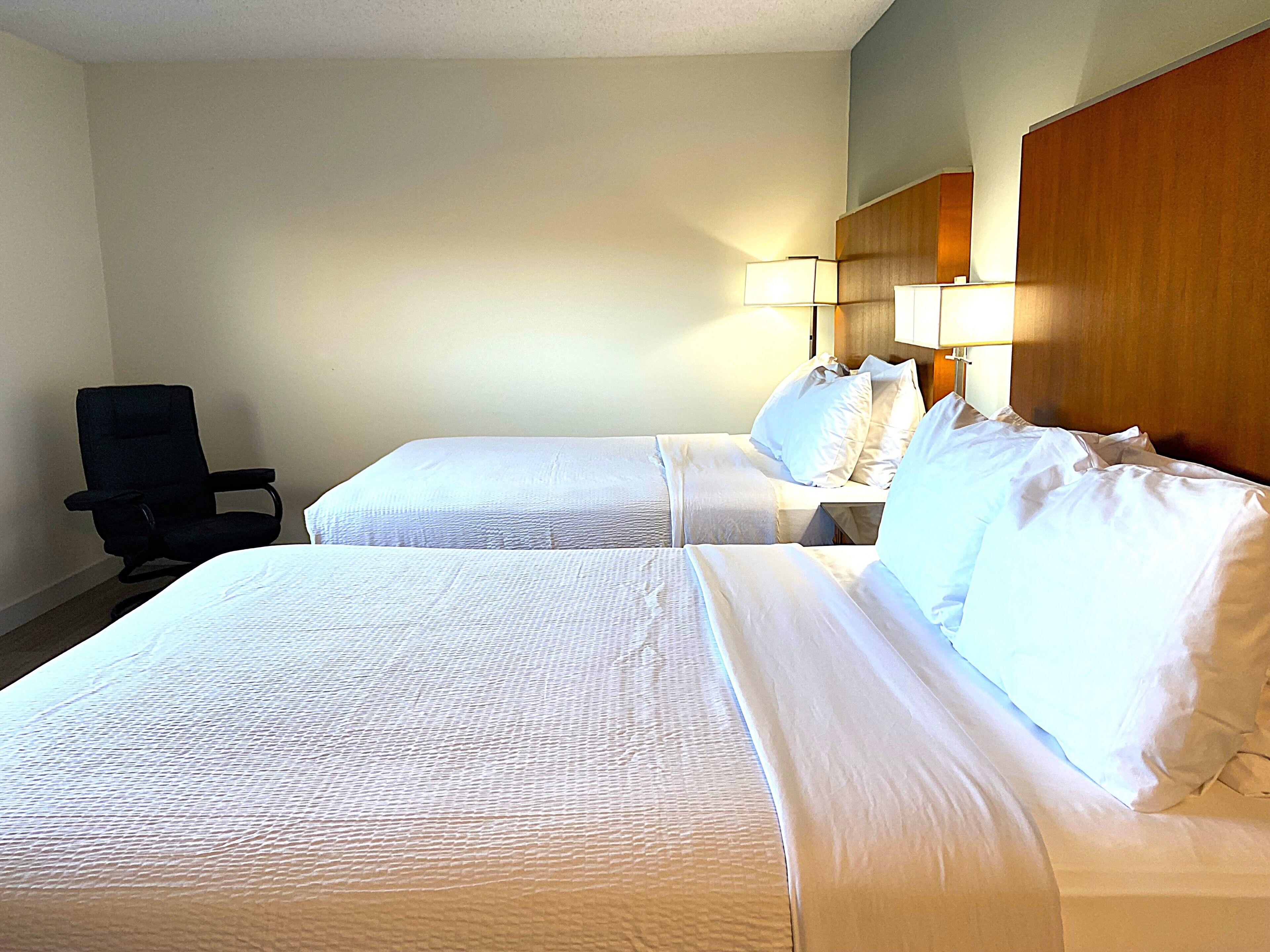 A hotel room with two beds, a chair, and a nightstand with lamps.