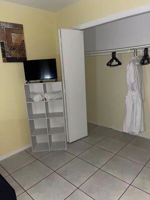 A room with a white wardrobe, a television on a stand, and a clothing rack with a white robe. - Cozy 2-bedroom house in pleasant Lauderhill with AC (Lauderhill)