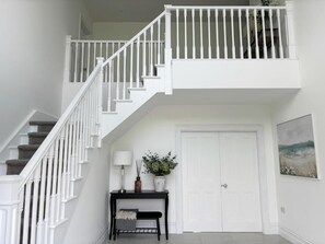 A staircase with white railings leading to a landing, a door, and a small console table with a lamp and a plant. - Eastbury House (Garryvoe)
