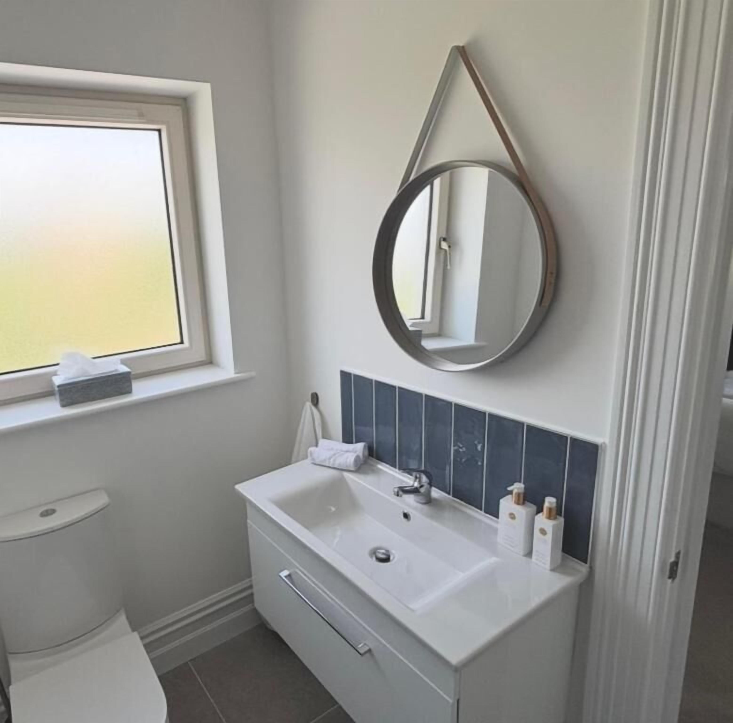 A bathroom with a white sink, a mirror, and a window.