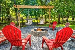 Un espace circulaire aménagé avec des sièges et un foyer, entouré de chaises rouges et d’une pergola en bois décorée de guirlandes lumineuses.
