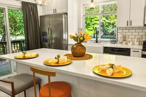 Een moderne keuken met een centraal eiland, roestvrijstalen apparatuur en uitzicht op groen.