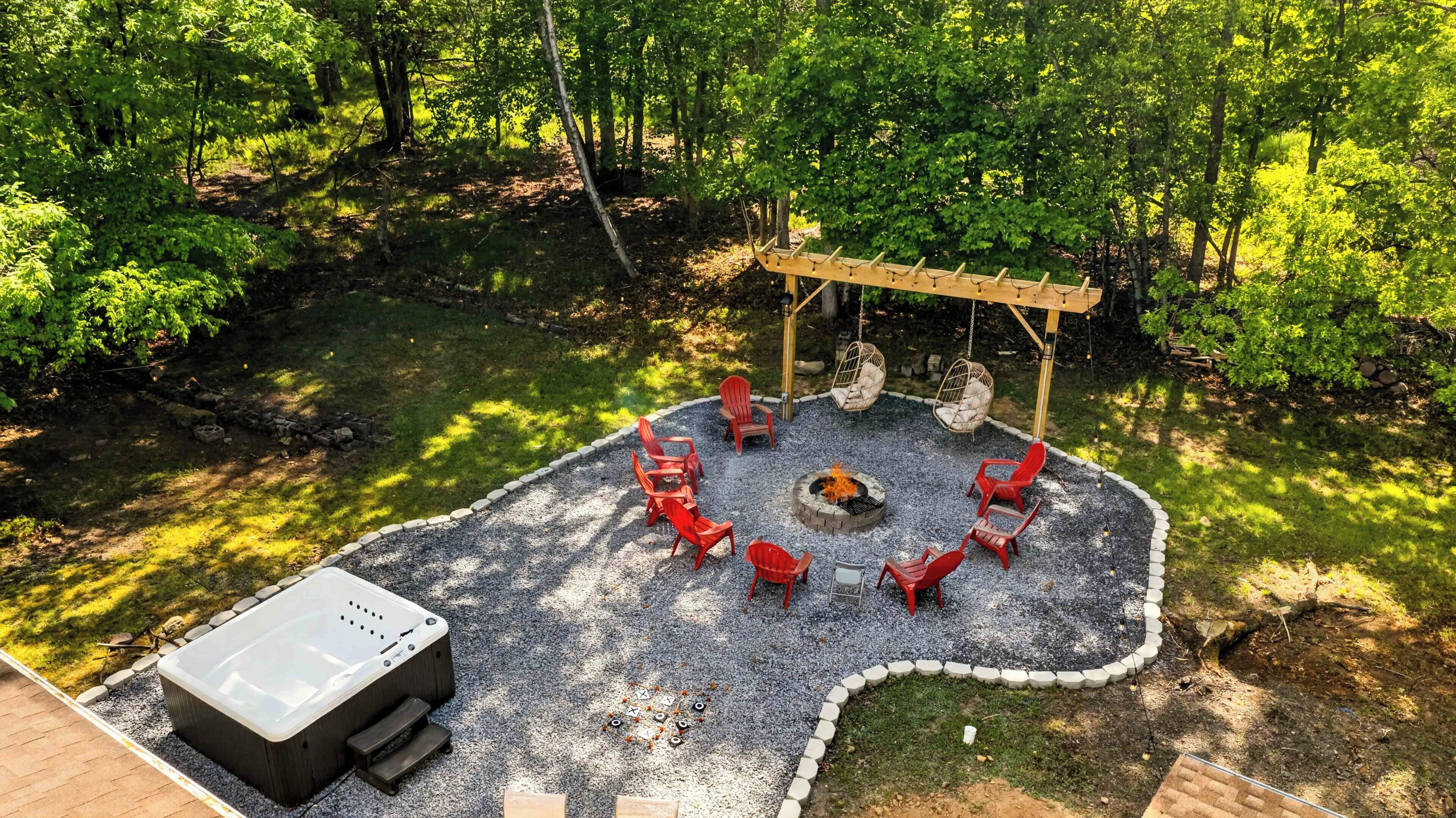 A circular outdoor seating area with a fire pit, surrounded by red chairs and a wooden pergola.