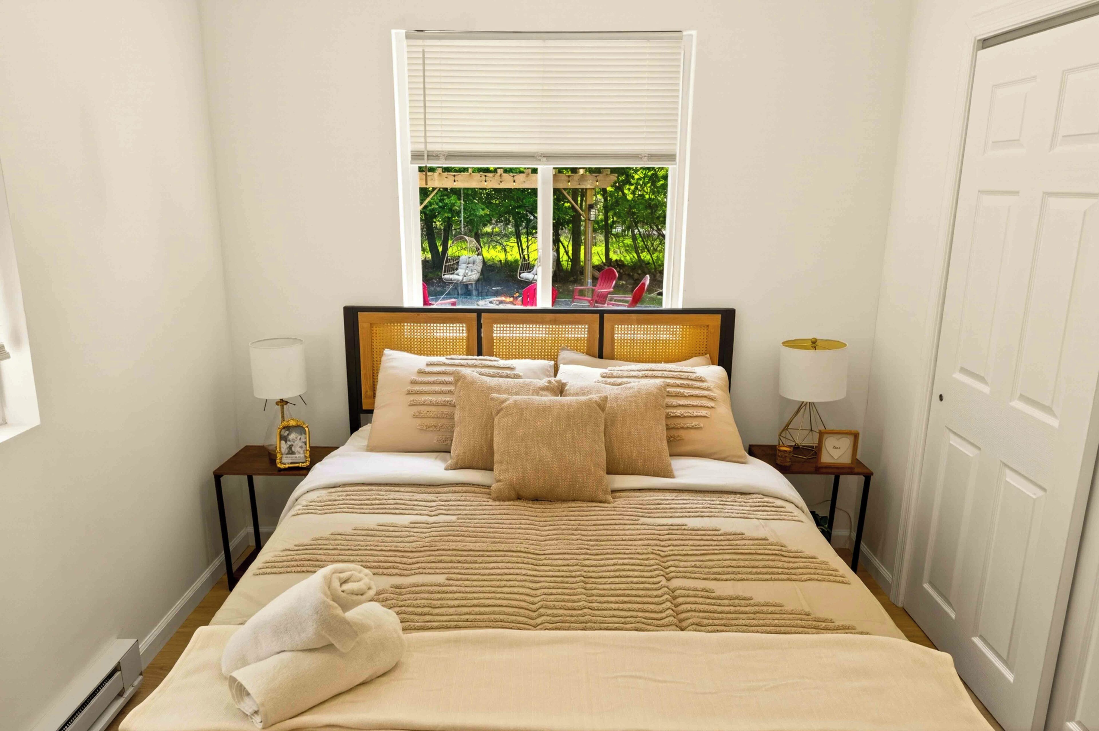 A neatly made bed with a striped blanket, two bedside lamps, and a window with a view of greenery.